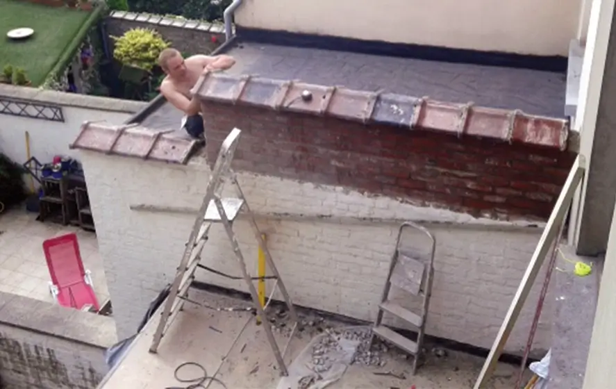 Photo d'un ouvrier qui rehausse un mur le long d'une terrasse.