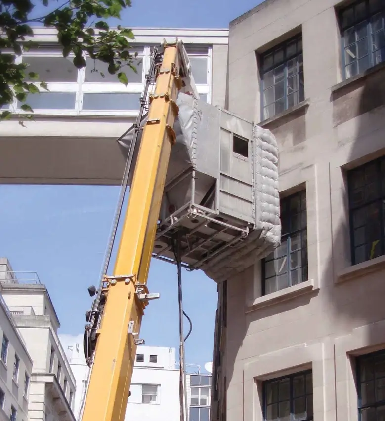 Photo d'une cabine de gommmage soutenue par une grue le long d'une façade