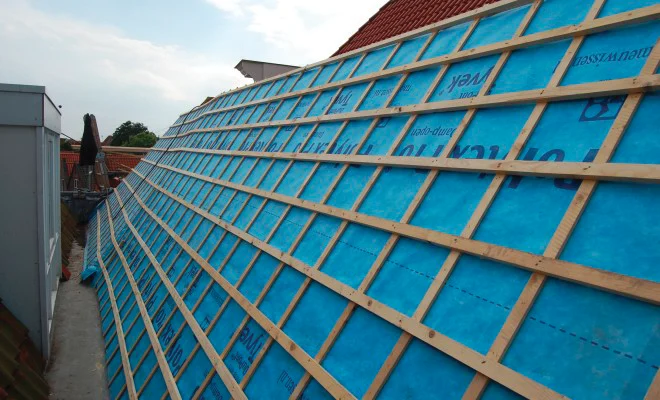 Toiture inclinée avec une sous-toiture souple de couleur bleue posée sur les chevrons, recouverte d’un lattage et d’un contre-lattage en bois avant la pose de la couverture.