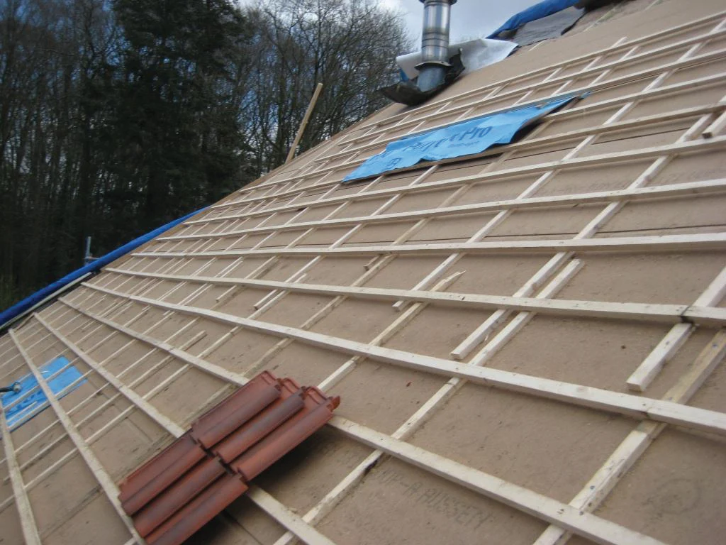 Toiture inclinée en cours de rénovation montrant une sous-toiture rigide posée sur les chevrons, avec un lattage et un contre-lattage en bois avant la pose des tuiles.